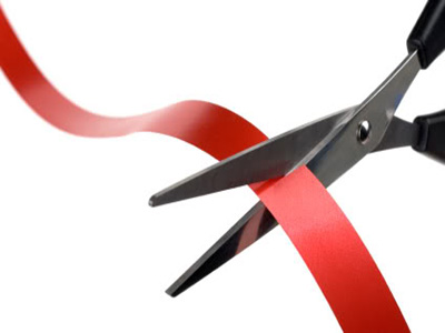 Closeup image of scissors cutting a red ribbon.